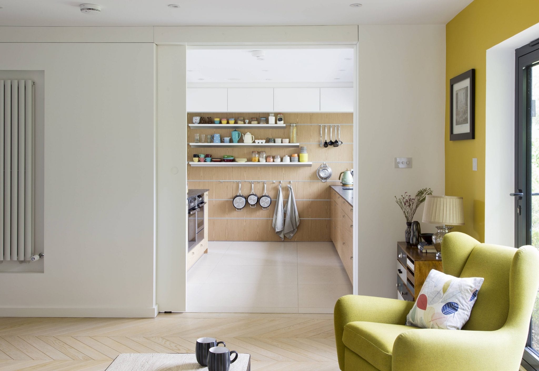 bright statement wall in the lounge highlights the yellow sofa that sits at the entrance of the kitchen