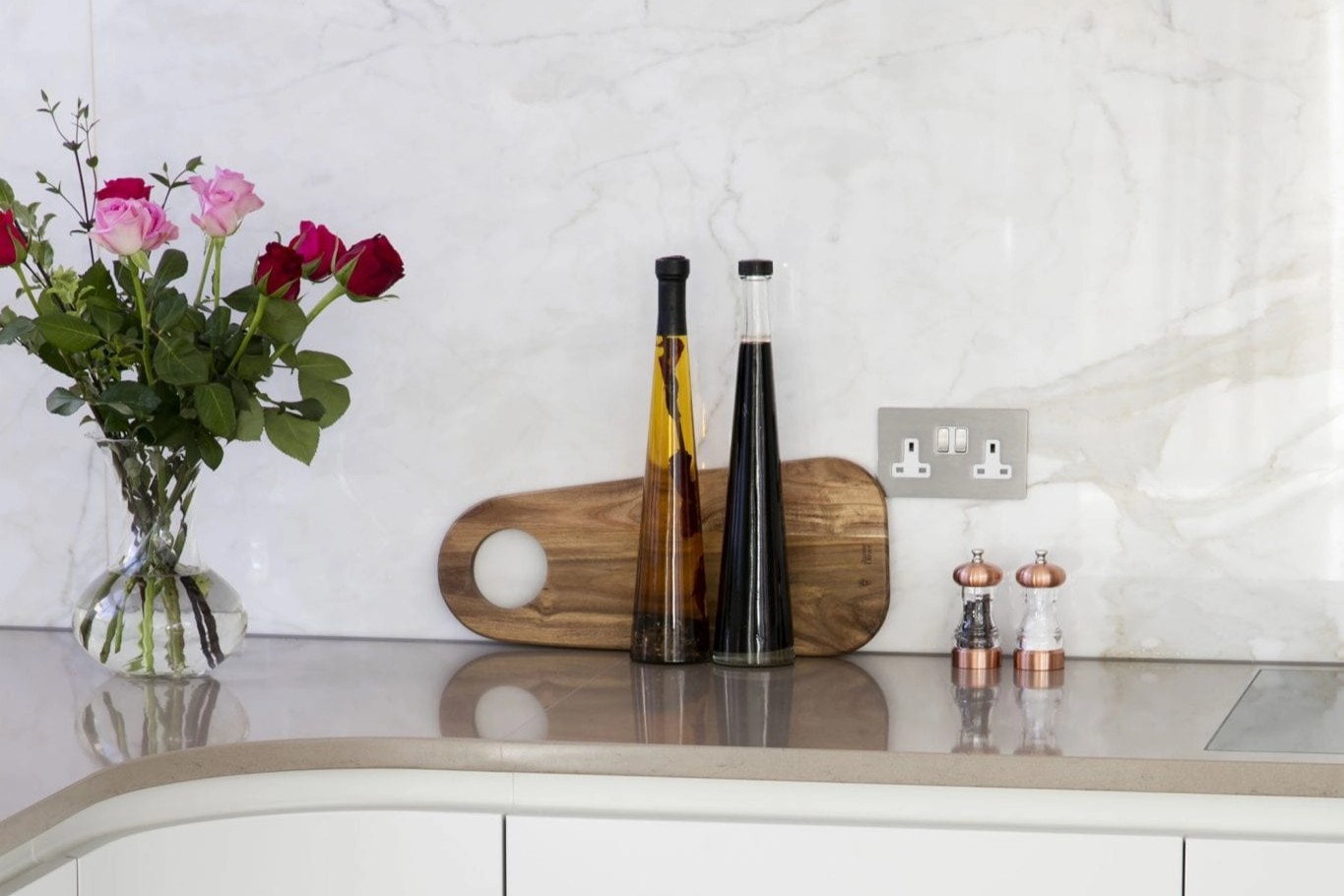 Contemporary kitchen worktop with pale stone splashback, white cabinetry and decorative accessories.